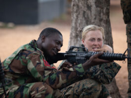 European woman teaching an African man how to shoot and kill other Africans... A mercenary under training. You've been invaded!
